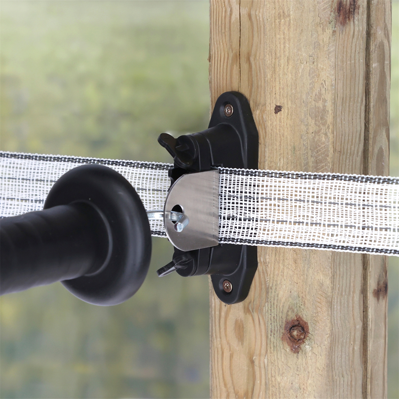 Doppelklicken zum vergrößern Nahaufnahme eines Kerbl 3x Kombi-Torgriffisolator „Profi“ für T-Abtrennungen an Streckenpfahl und Ecken. Abbildung des an einem Holzpfahl angeschraubten Isolators, der ein Weidezaunband führt und in dessen Vorrichtung ein Torgriff eingehängt ist.