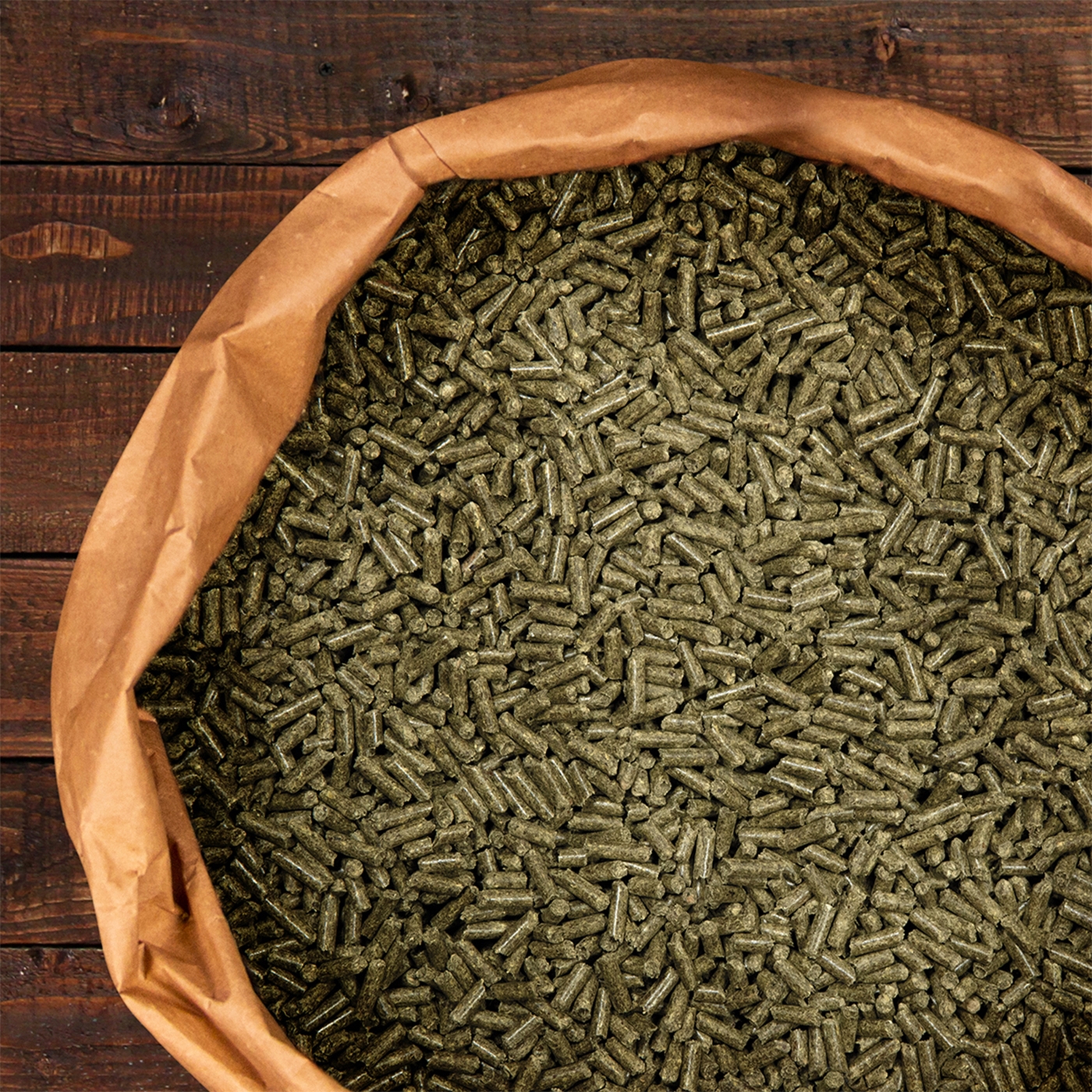Ein geöffneter Sack mit grünlichen Tierfutterpellets liegt auf einer Holzunterlage.