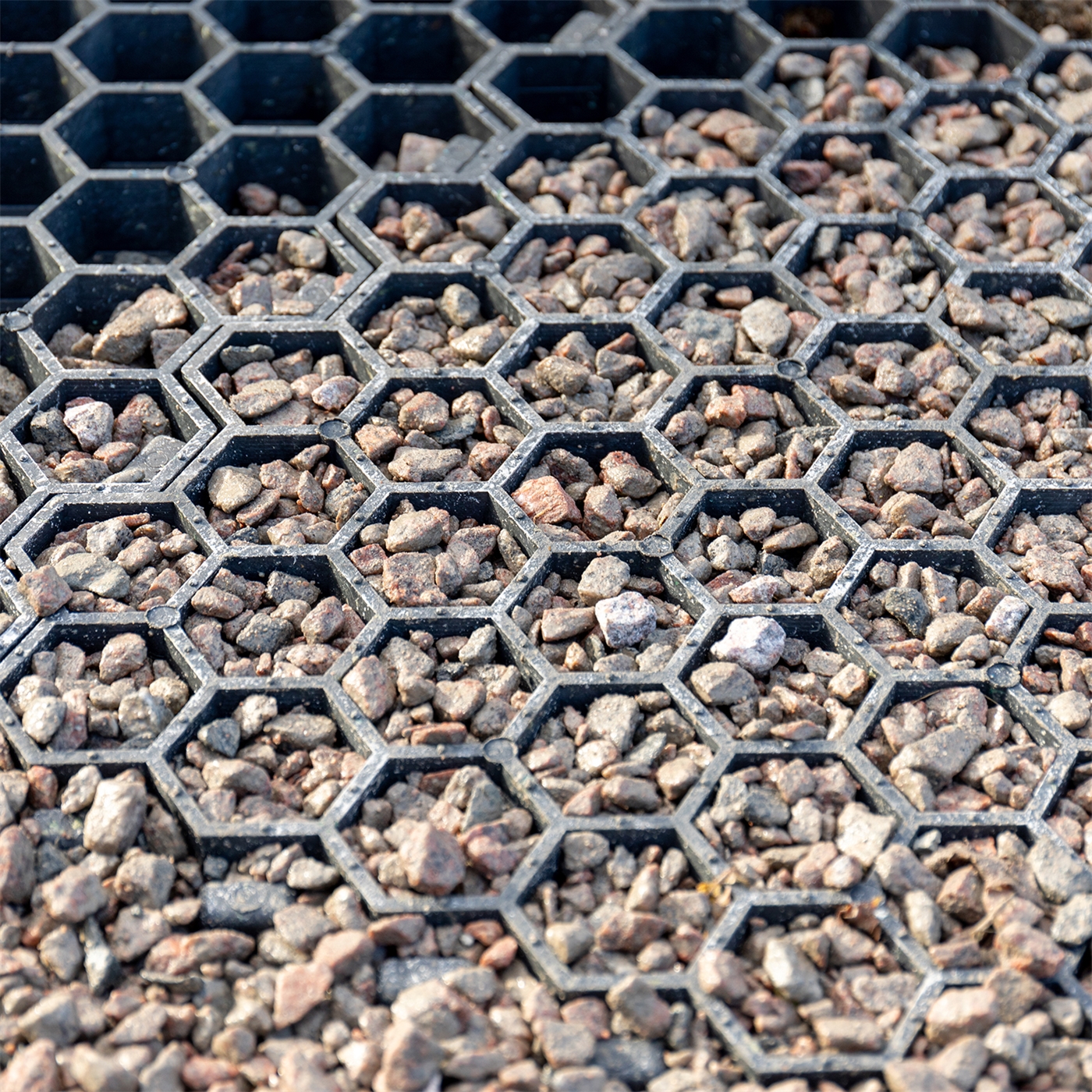 Doppelklicken zum vergrößern Nahaufnahme kleiner Steine in einer VOSS.farming Paddockplatte Rasengitter Paddockgitter (50 x 40 x 4 cm), einem schwarzen sechseckigen Kunststoffgitter zur Bodenstabilisierung.