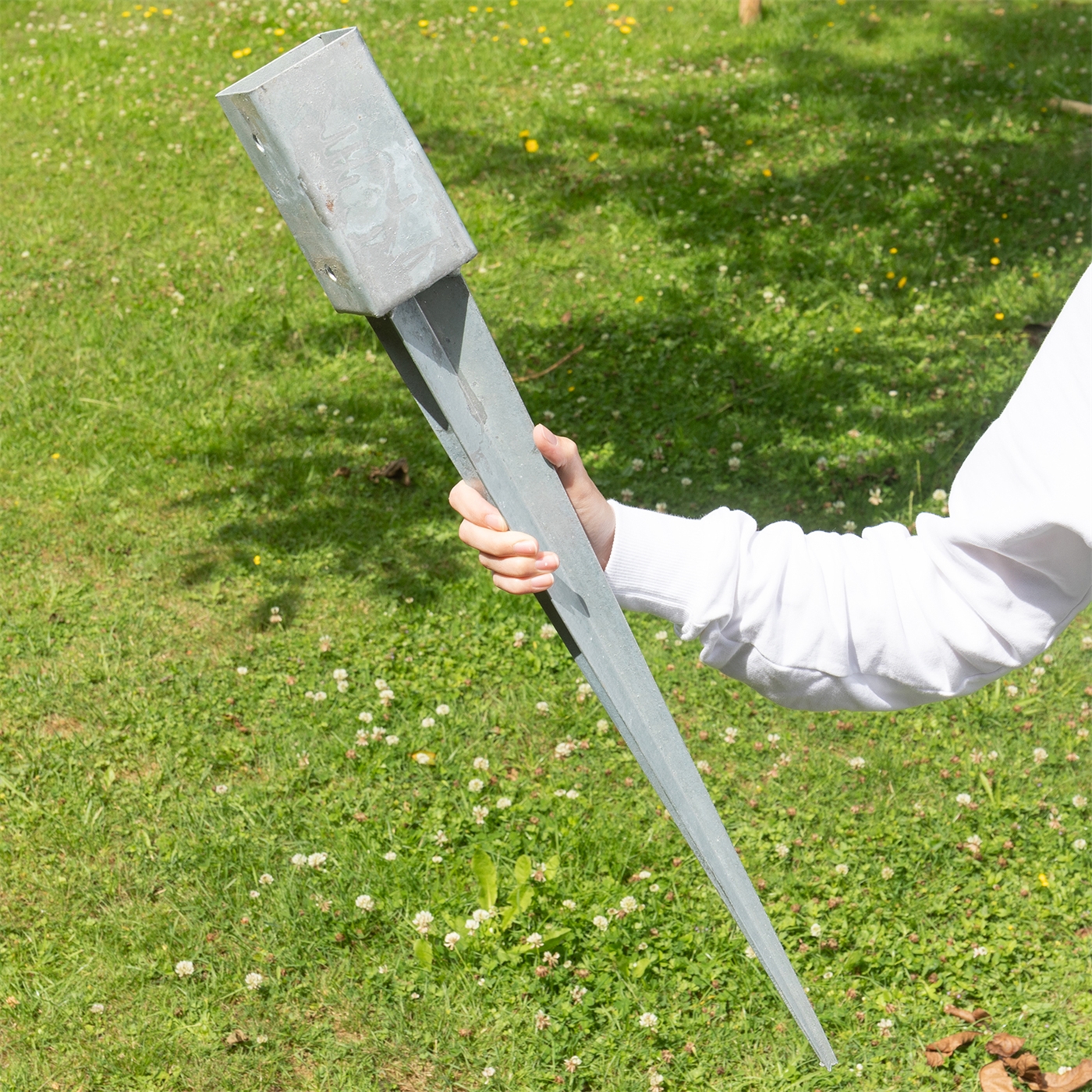 Eine Person hält eine Bodeneinschlaghülse, Metall, 7 x 7 x 75cm über Gras.