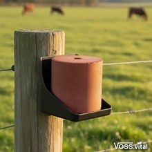 VOSS.vital Leckstein - MineralLine Salzleckstein mit Spurenelementen 5kg von S.I.N. Hellas auf einem Zaunpfosten im Feld, während im Hintergrund Pferde grasen.