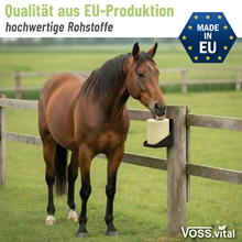 Ein braunes Pferd frisst aus einem Futterautomaten an einem Holzzaun auf einer Wiese; abgebildet sind die S.I.N. Hellas VOSS.vital Leckstein - BiotinLine mit Biotin & Vitamin E 5kg und die dazugehörigen Logos.