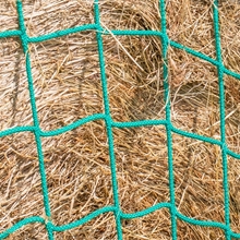 Ein grünes VOSS.farming-Netz mit quadratischen Maschen – Rahmen für Futtersparnetz – für quadratische Futterraufen, 1,68 m x 1,68 m, verzinkt, über trockenes Heu gespannt.
