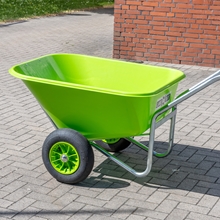 Die LandXpert Schubkarre (250 Liter, grün, mit Doppelbereifung, Kunststoffwanne, Luftreifen) von LandXpert ist mit schwarzen Reifen auf einem gepflasterten Untergrund in der Nähe einer roten Backsteinmauer abgebildet.