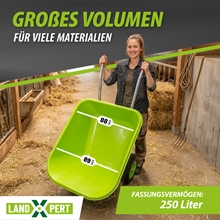 Eine Frau steht in einer Scheune, lächelt in die Kamera und hält eine LandXpert-Schubkarre – 250 Liter, grün, mit Doppelbereifung, Kunststoffwanne und Luftreifen – in der Hand.