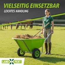 Eine Frau steht auf einer Wiese mit einer LandXpert Schubkarre 250L grün, doppelt bereift (Kunststoffwanne, Luftreifen), die mit Heu beladen ist, während im Hintergrund Pferde grasen.