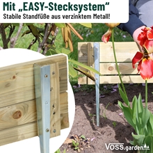 Der VOSS.garden Steckzaun 75x18cm, eine Garteneinfassung aus Holz mit Metallpfosten, wird hier als VOSS.garden Beeteinfassung zwischen Pflanzen und Blumen eingesetzt.
