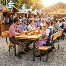 Bei einer festlichen Veranstaltung im Freien genießen die Gäste in bayerischer Tracht Bier und Speisen auf der VOSS.garden Bierzeltgarnitur mit Rückenlehne 170cm, einem faltbaren Holztisch mit Sitzbank von VOSS.garden.