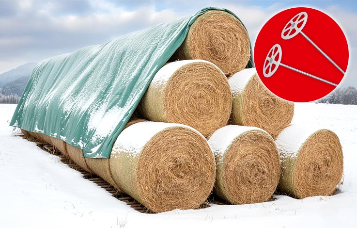 Auf einer verschneiten Weide stehen Heuballen mit einem Heuvlies überdeckt